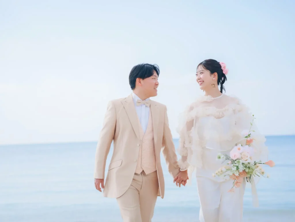 沖縄の美らSUNビーチで撮影したロケーションフォトウェディング。青い海と空の下で手をつなぐ新郎新婦。