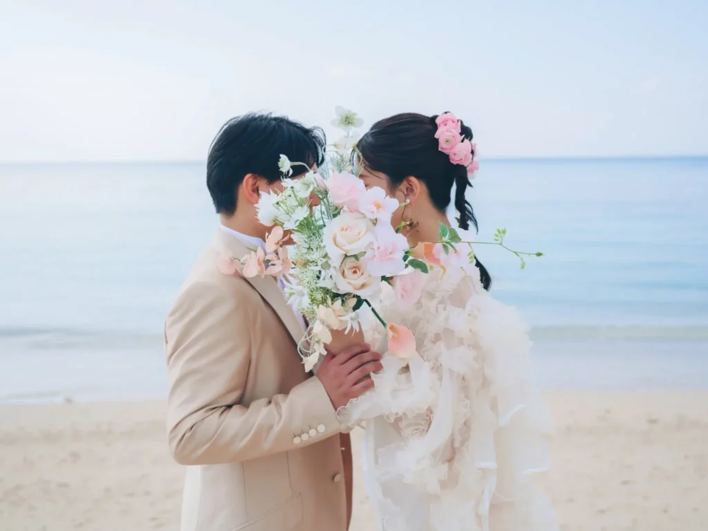 沖縄の美らSUNビーチで撮影したロケーションフォトウェディング。青い海の前で花束をもつ新郎新婦。