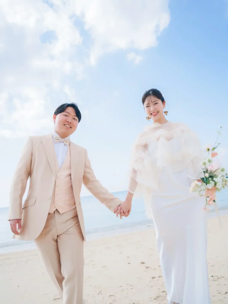 沖縄の美らSUNビーチで撮影したロケーションフォトウェディング。青い海と空の下で手をつなぐ新郎新婦。